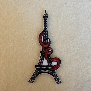 Peut inclure: Patch thermocollant brodé en noir et blanc de la tour Eiffel avec un ruban rouge enroulé autour.