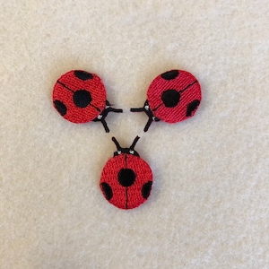 Könnte beinhalten: Drei rote Marienkäfer-Stoffapplikationen mit schwarzen Punkten und weißen Akzenten.