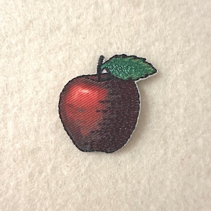 May include: Embroidered apple patch with a red gradient and a green leaf. The apple has a detailed texture and a black outline. This patch is suitable for clothing, bags, or other fabric items.