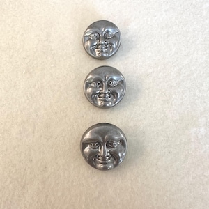 Può includere: Tre bottoni rotondi color argento con un design a faccina sorridente. I bottoni hanno un aspetto vintage e antico. I volti hanno tratti dettagliati, tra cui occhi, naso e bocca sorridente. I bottoni sono probabilmente per cucito o artigianato.