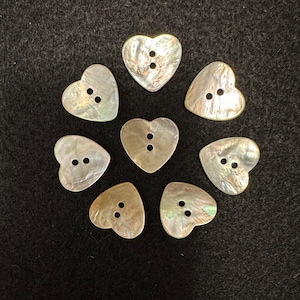 Può includere: Otto bottoni a forma di cuore di colore bianco iridescente con due fori ciascuno.
