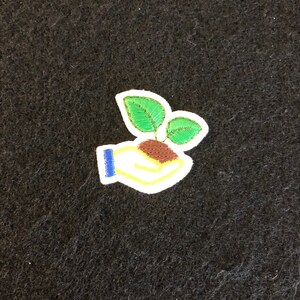 May include: A white hand with blue and yellow accents holding a small green plant with brown roots.