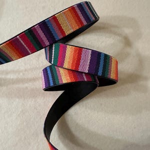 May include: A colorful striped fabric strap with a black backing. The strap is folded and twisted, showing the different colors of the fabric.