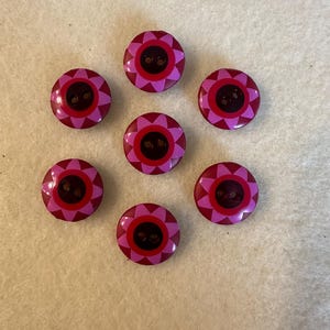 Puede incluir: Siete botones rosas y rojos con un diseño de flores. Los botones tienen dos agujeros.