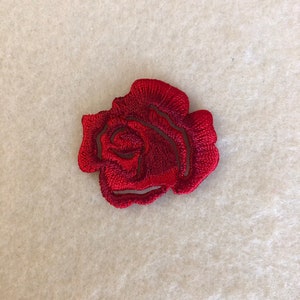 Puede incluir: Un parche de rosa bordado en rojo. La rosa es un diseño floral clásico.