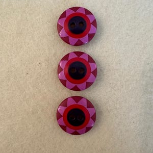 Può includere: Tre bottoni rotondi con un designo a fiore rosa e rosso e un centro nero. I bottoni hanno due fori.