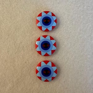May include: Three red buttons with a blue and white starburst design. The buttons have a dark blue center with a smaller red circle in the center.