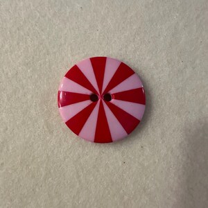 Könnte beinhalten: Ein rosa-roter gestreifter Knopf mit zwei Löchern in der Mitte.
