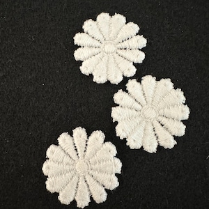 Może przedstawiać: Trzy białe haftowane aplikacje kwiatowe na czarnym tle.