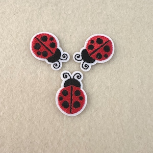 Może przedstawiać: Trzy haftowane naszywki w kształcie biedronek. Każda biedronka ma czerwone ciało z czarnymi kropkami, czarną głowę i białą obwódkę. Biedronki ułożone są w trójkąt na neutralnym tle.