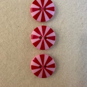 Puede incluir: Tres botones rayados de color rosa y rojo con dos agujeros cada uno.