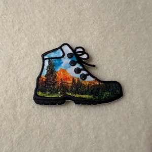 May include: A white hiking boot with a colorful mountain scene printed on the side. The boot has black laces and a black sole.