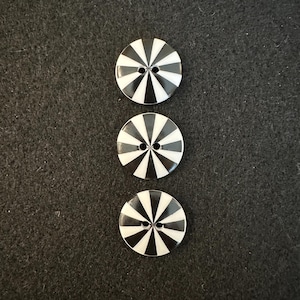 May include: Three black and white striped buttons with two holes each. The buttons are arranged vertically in a row.