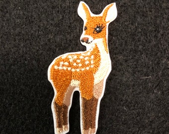 以下が含まれることがあります： 茶色と白の斑点のある子鹿の刺繍アイロン接着パッチ。子鹿は4本足で立っており、白い背景です。