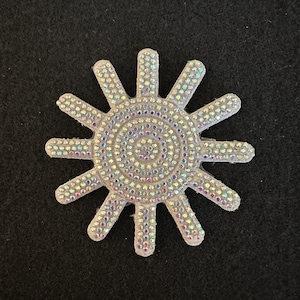 May include: A white sun-shaped patch with a circular design of iridescent rhinestones in the center. The sun has 10 points.