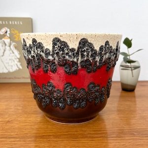 May include: A ceramic planter with a textured, lava-like design. The top rim is cream-colored, followed by a band of black, a vibrant red section, and a dark brown base. The planter is suitable for indoor plants.