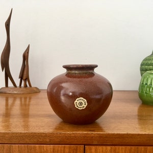 以下が含まれることがあります： 丸いボディとわずかに広がった縁を持つ茶色の陶器の花瓶。花瓶の底には「Steuler Keramik」と書かれたラベルが付いています。