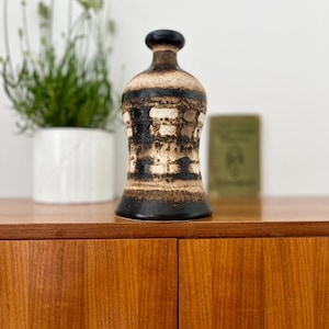 Könnte beinhalten: Eine Vintage-Keramikvase mit einem dunkelbraunen und beigefarbenen geometrischen Muster. Die Vase hat eine bauchige Form mit schmalem Hals und einem dunkelbraunen Oberteil. Die Vase steht auf einer Holzoberfläche.