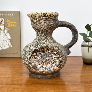 Peut inclure: Pichet en céramique vintage avec un glaçage moucheté marron et beige. Le pichet a un corps arrondi, un col étroit et une grande anse incurvée. Le bord est de couleur beige clair. Un objet décoratif pour la maison.