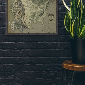 May include: A framed vintage map of the United States with a green and brown color scheme. The map shows the states and major cities. The map is framed in a dark wood frame. The map is hanging on a black brick wall. A potted plant is on a wooden stool in the corner of the room.