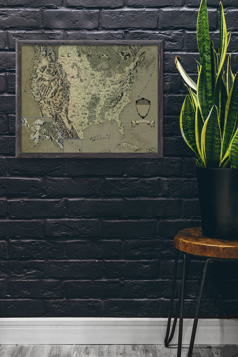 May include: A framed vintage map of the United States with a green and brown color scheme. The map shows the states and major cities. The map is framed in a dark wood frame. The map is hanging on a black brick wall. A potted plant is on a wooden stool in the corner of the room.