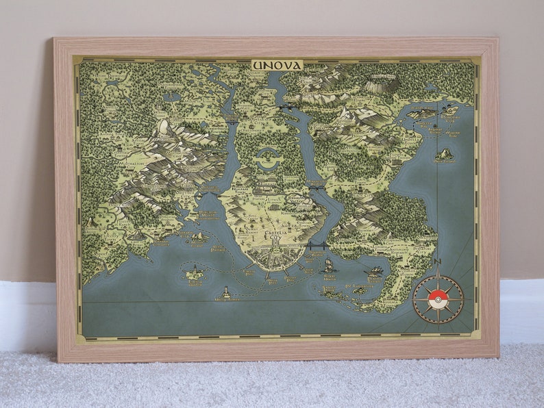 May include: A vintage-style map of the Unova region from the Pokemon video game series. The map is framed in a light wood frame and features a compass with the Pokemon logo in the bottom right corner. The map shows the various cities, towns, and routes of the region.