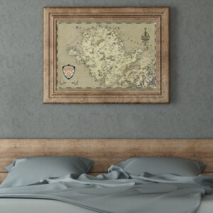May include: A framed map of a fictional island with a coat of arms in the bottom left corner. The map is in a rustic wooden frame and is hanging on a gray wall above a bed with a wooden headboard and blue bedding.