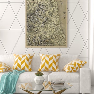 May include: A white couch with yellow and white patterned throw pillows, a blue throw blanket, and a glass coffee table with a stack of books. A framed vintage map of a coastline with the text "North Sea" is hanging on the wall behind the couch.