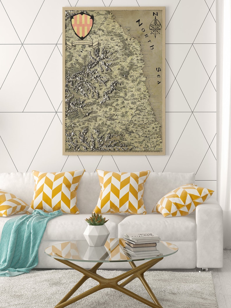 May include: A white couch with yellow and white patterned throw pillows, a blue throw blanket, and a glass coffee table with a stack of books. A framed vintage map of a coastline with the text "North Sea" is hanging on the wall behind the couch.