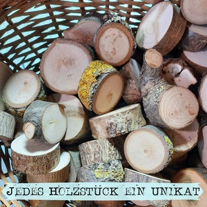 May include: A basket filled with various wooden slices, showcasing natural wood grain and bark textures. The pieces vary in size and shape, with some displaying yellow and green lichen. The text "JEDES HOLZST&Uuml;CK EIN UNIKAT" is visible at the bottom.