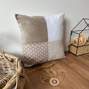 Op de afbeelding: Een vierkant kussen met een patchwork ontwerp. Het kussen is gemaakt van vier verschillende stoffen: corduroy, wit met kleine zwarte stippen, beige met witte stippen en een wafelstof. Het kussen is beige, wit en bruin.