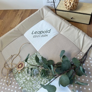 Może przedstawiać: Kocyk dla niemowlęcia w patchworku w kolorze beżowym i białym z zielonym wzorem kwiatowym i wyhaftowanym imieniem "Leopold" oraz datą "03.01.2024".