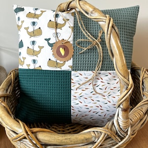 Può includere: Un cuscino in patchwork verde e bianco con un motivo a balena e pesce. Il cuscino è in un cesto di vimini.