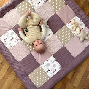 Könnte beinhalten: Ein Baby liegt auf einer Patchwork-Spielmatte mit verschiedenen Mustern, darunter Blumen, Punkte und einfarbige Farben. Die Matte besteht aus weichem, gestepptem Stoff und ist perfekt für die Bauchzeit oder zum Spielen.
