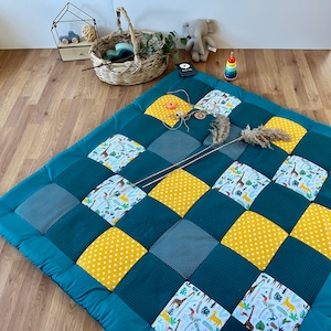Könnte beinhalten: Eine türkisblaue und gelbe Patchwork-Spielmatte mit Giraffenmuster, Punkten und einfarbigen Stoffquadraten. Die Matte ist perfekt für Babys und Kleinkinder zum Spielen.