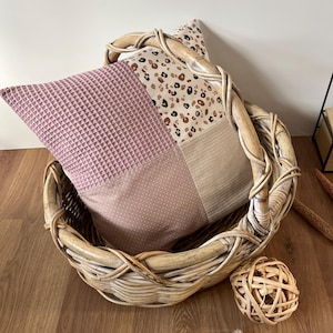 May include: A pink and beige patchwork pillow with a brown and white animal print design sits in a woven wicker basket.