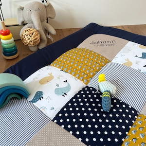 Könnte beinhalten: Eine marineblaue und beige Baby-Spielmatte mit verschiedenen Mustern, darunter Wale, Regenbögen und Punkte. Die Matte ist mit dem Namen "Johann" und dem Datum "15.08.2022" personalisiert.