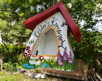 Puede incluir: Una casita de pájaros blanca con un techo rojo y un diseño pintado de flores, mariposas y el texto "Richter's Koheparty".