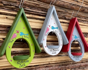 Pode incluir: Três comedouros de pássaros de madeira pintados em cores diferentes, verde, cinza e vermelho. Cada comedouro tem uma abertura em forma de coração com um pequeno pássaro pintado nele. Os comedouros são decorados com os nomes dos casais e as datas dos seus aniversários de casamento. As datas são 12 de outubro de 2022, 8 de dezembro de 2022 e 23 de novembro de 2022.
