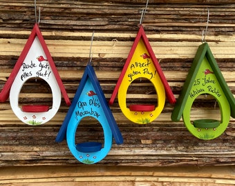 Pode incluir: Quatro comedouros para pássaros coloridos com diferentes ditos. Os comedouros são pintados em vermelho, azul, amarelo e verde. Os ditos são "Rente gut, Alles gut!" "Opa Ottos Meisenbar" "Allzeit guten Flug!" e "25 Jahre Holzban Richter".