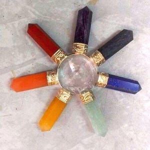 Peut inclure: Un générateur d'énergie en cristal avec une sphère centrale en quartz clair, entourée de sept pointes de cristal colorées : rouge, orange, jaune, vert, bleu, indigo et violet. Chaque cristal est serti dans une base métallique dorée.