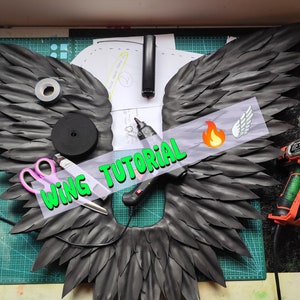 May include: A black foam wing with a wing tutorial text overlay. The image shows the supplies needed to make the wings, including a heat gun, scissors, and glue gun.