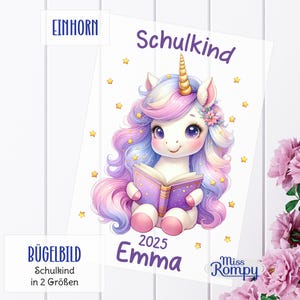 Könnte beinhalten: Eine Illustration eines Einhorns, das ein Buch liest, mit einem lila Einband und goldenen Sternen. Das Einhorn hat ein goldenes Horn, rosa und lila Haare und ist von goldenen Sternen umgeben. Der Text "Schulkind 2025 Emma" ist ebenfalls vorhanden.