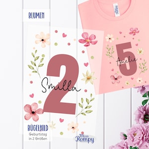 Könnte beinhalten: Ein hellrosa T-Shirt mit einer großen dunkelrosa Zahl 5 und dem Namen Amelie in schwarzer Schreibschrift, umgeben von Aquarellblumen, Blättern und kleinen Herzen. Daneben zeigt eine transparente Folie eine Zahl 2 mit dem Namen Smilla.
