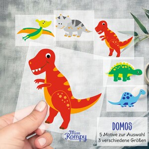Peut inclure: Cinq autocollants de dinosaures colorés avec le texte "DOMOS 5 Motive zur Auswahl 3 verschiedene Größen" et le logo "Miss Rompy".