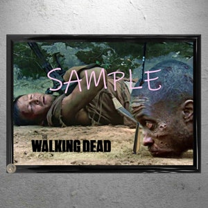 Puede incluir: Un póster enmarcado con una escena de "The Walking Dead". La imagen muestra a un hombre en el suelo con un arma y una cabeza cortada. La palabra "SAMPLE" está escrita en la parte superior de la imagen.