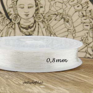 Könnte beinhalten: Eine Spule mit klarem elastischem Band, 0,8 mm dick, zum Schmuck basteln.
