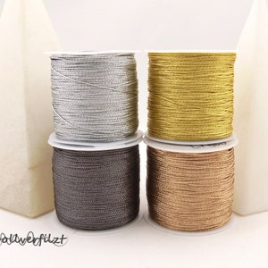 Könnte beinhalten: Vier Spulen mit Metallic-Garn in Silber, Gold, Grau und Braun.