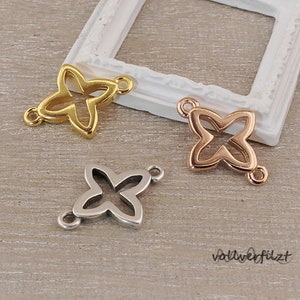 Könnte beinhalten: Drei Metall-Schmetterlingsanhänger in Gold, Roségold und Silber. Die Anhänger haben eine vierzackige Sternform mit einem offenen Zentrum.
