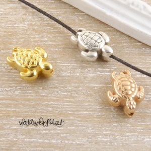 Könnte beinhalten: Drei Schildkröten-Anhänger in Gold, Silber und Roségold. Die Anhänger sind mit strukturierten Schalen verziert und perfekt für die Schmuckherstellung.